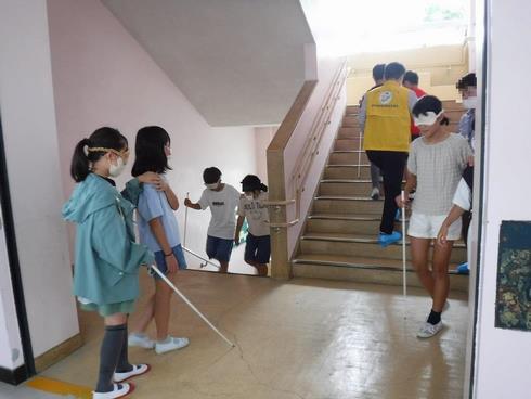 目隠しをした5年生が白杖を使って階段を上っています。介助するのも5年生です。