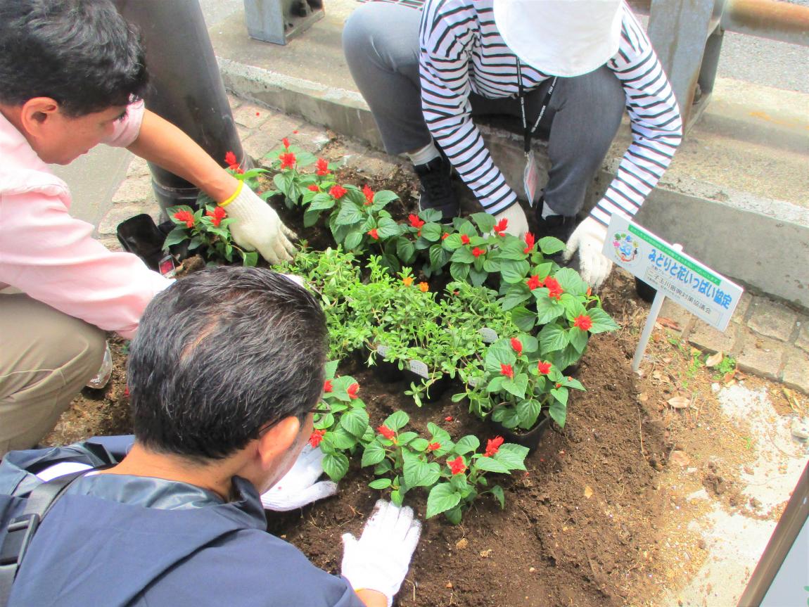 花壇を3人が囲み、協力して植えている様子。