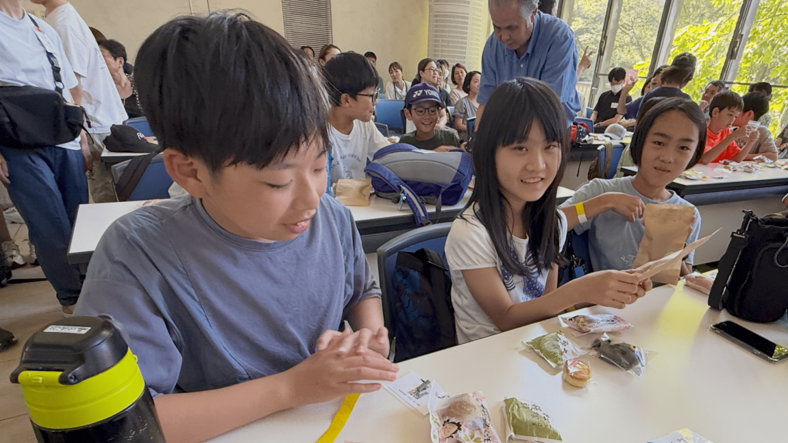 LEARNプログラム8「ミッションで購入したお菓子を他の班におすそ分けしている様子」