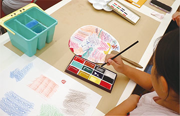 夏らしい絵をうちわに描く様子の写真