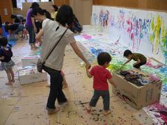 児童館の壁一面に張られた紙に絵の具でおもいっきり描く幼児